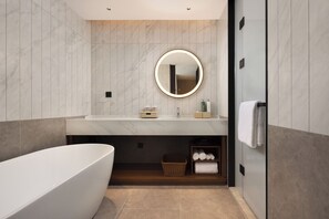 A modern bathroom with a freestanding bathtub, a round mirror with a light, a vanity with toiletries, and a towel rack. - Hilton Garden Inn Chengdu Jinsha Site Museum (Chengdu)