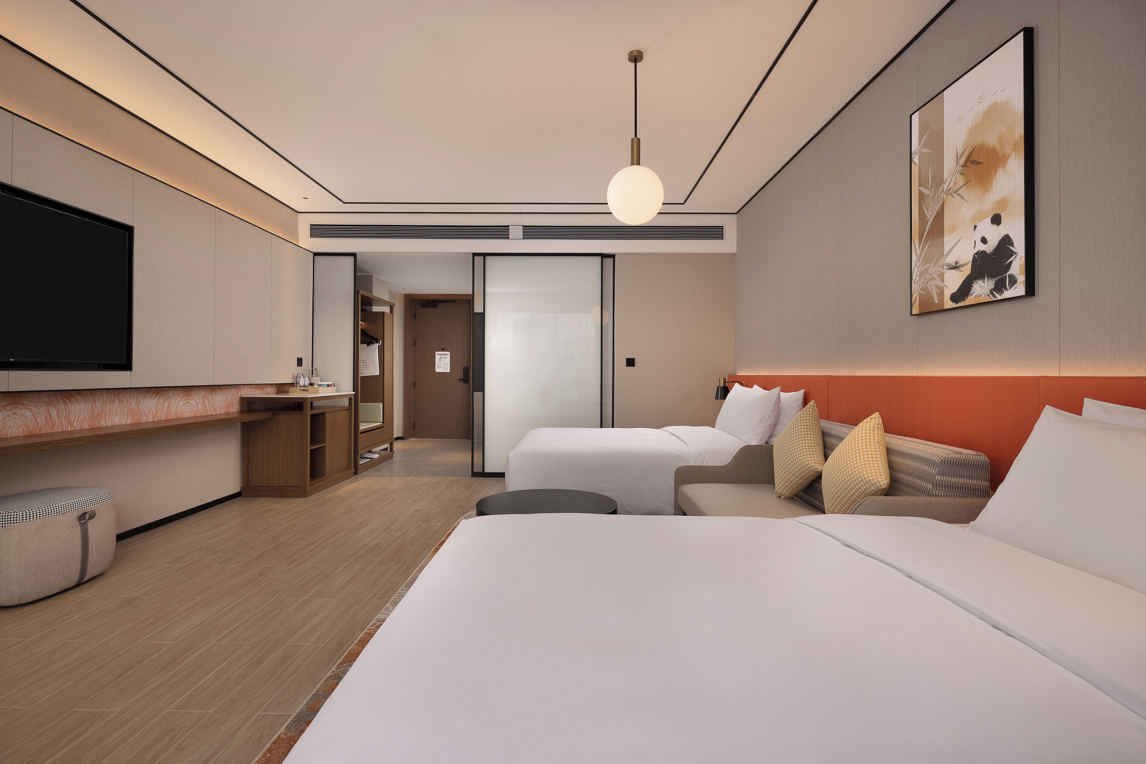 A modern hotel room with a large bed, a sofa, a TV, and a painting on the wall.