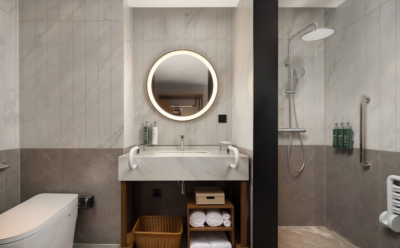 A modern bathroom with a round mirror, a sink, and a shower.