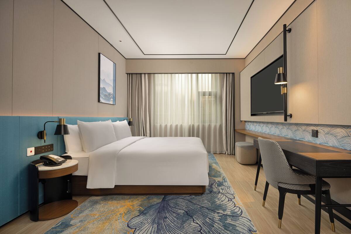 Una habitación de hotel con una cama grande, un escritorio, una silla, un teléfono y un televisor.