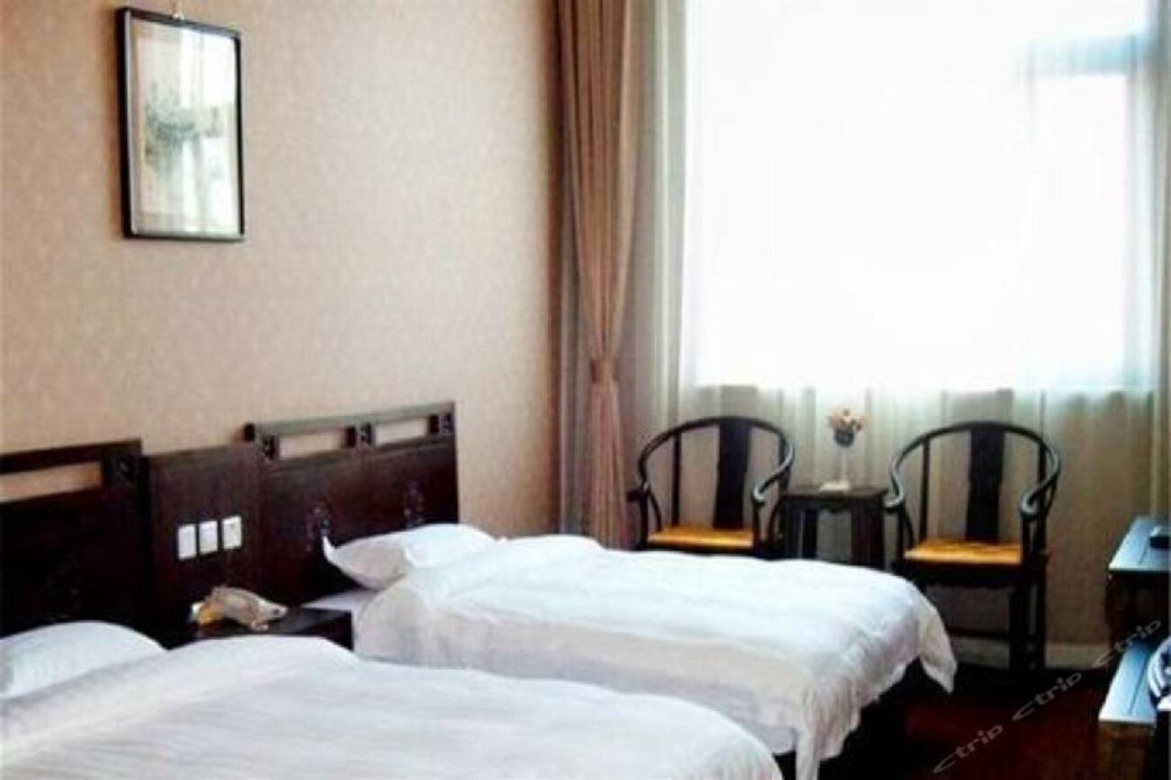 Una camera d'albergo con due letti singoli, un tavolino, due sedie e una finestra con tende.