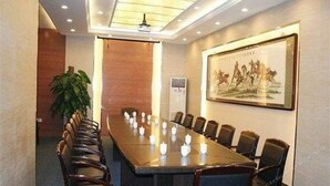 Une salle de conférence avec une longue table, des chaises, une plante et un tableau encadré au mur.