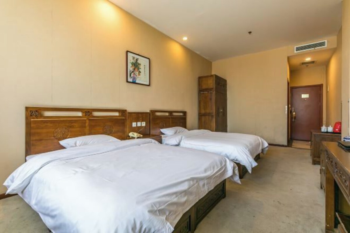 Une chambre d’hôtel avec deux lits, une tête de lit en bois, une table de chevet avec une lampe et un tableau encadré au mur.