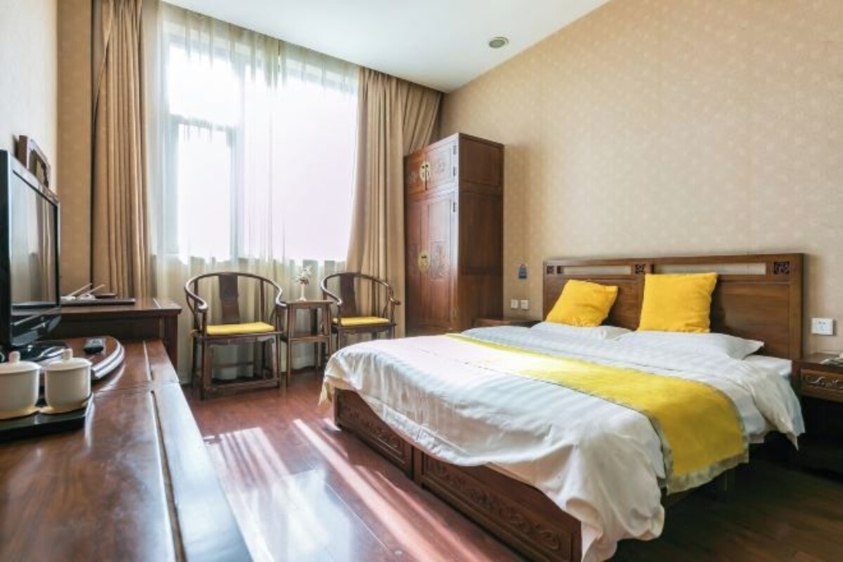 Une chambre d’hôtel avec un lit en bois, un bureau avec des chaises, une télévision et une armoire.