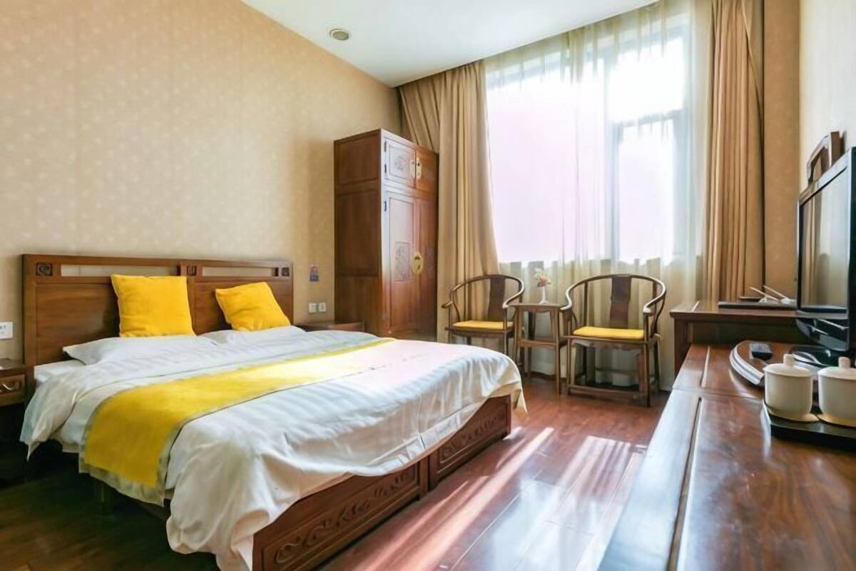 Une chambre d’hôtel avec un lit, une tête de lit en bois, deux chaises, un téléviseur et un meuble.