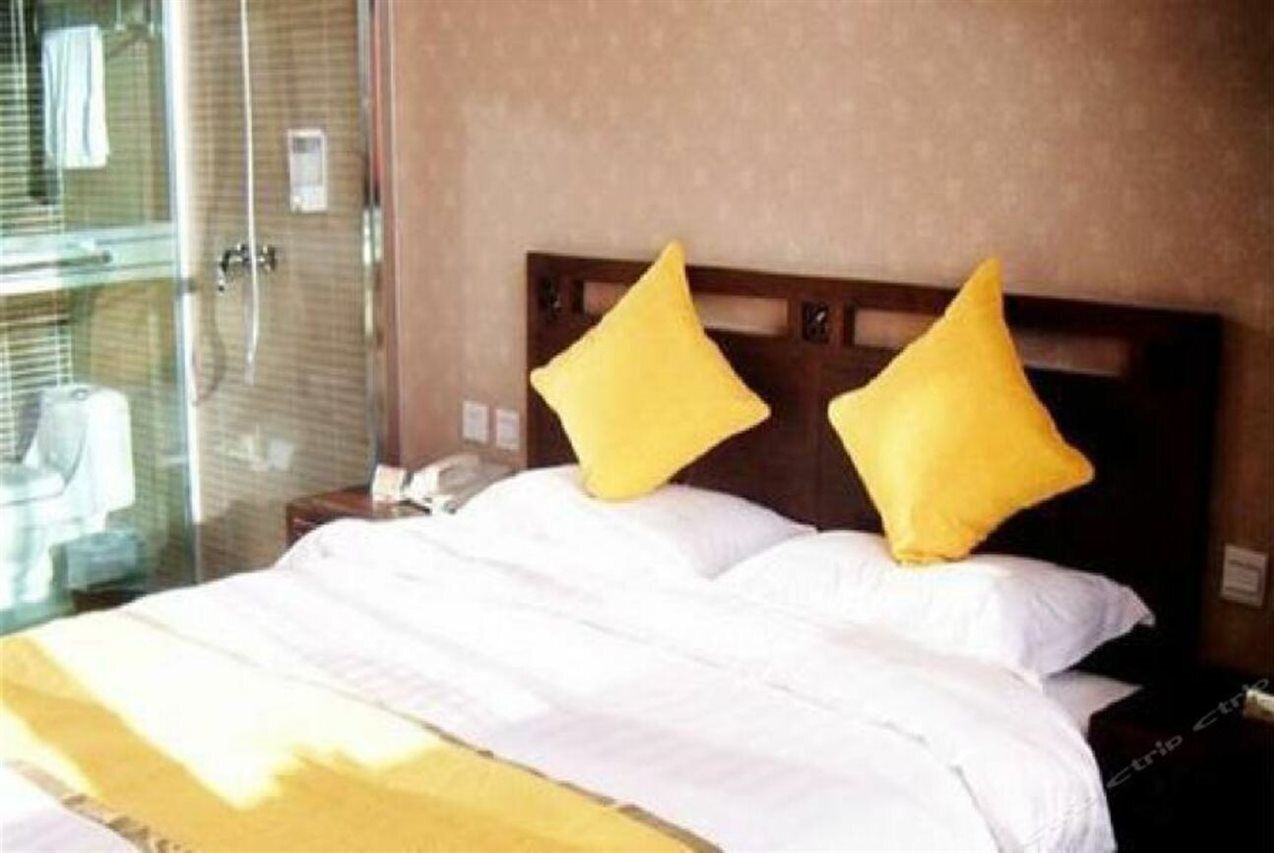 A hotel room with a bed, two pillows, a nightstand, and a glass shower enclosure.