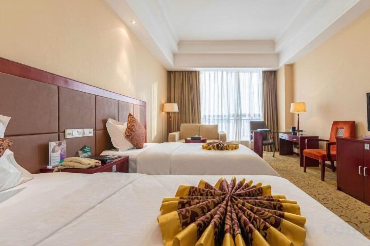 A hotel room with two beds, a desk, a chair, and a view of the outdoors.