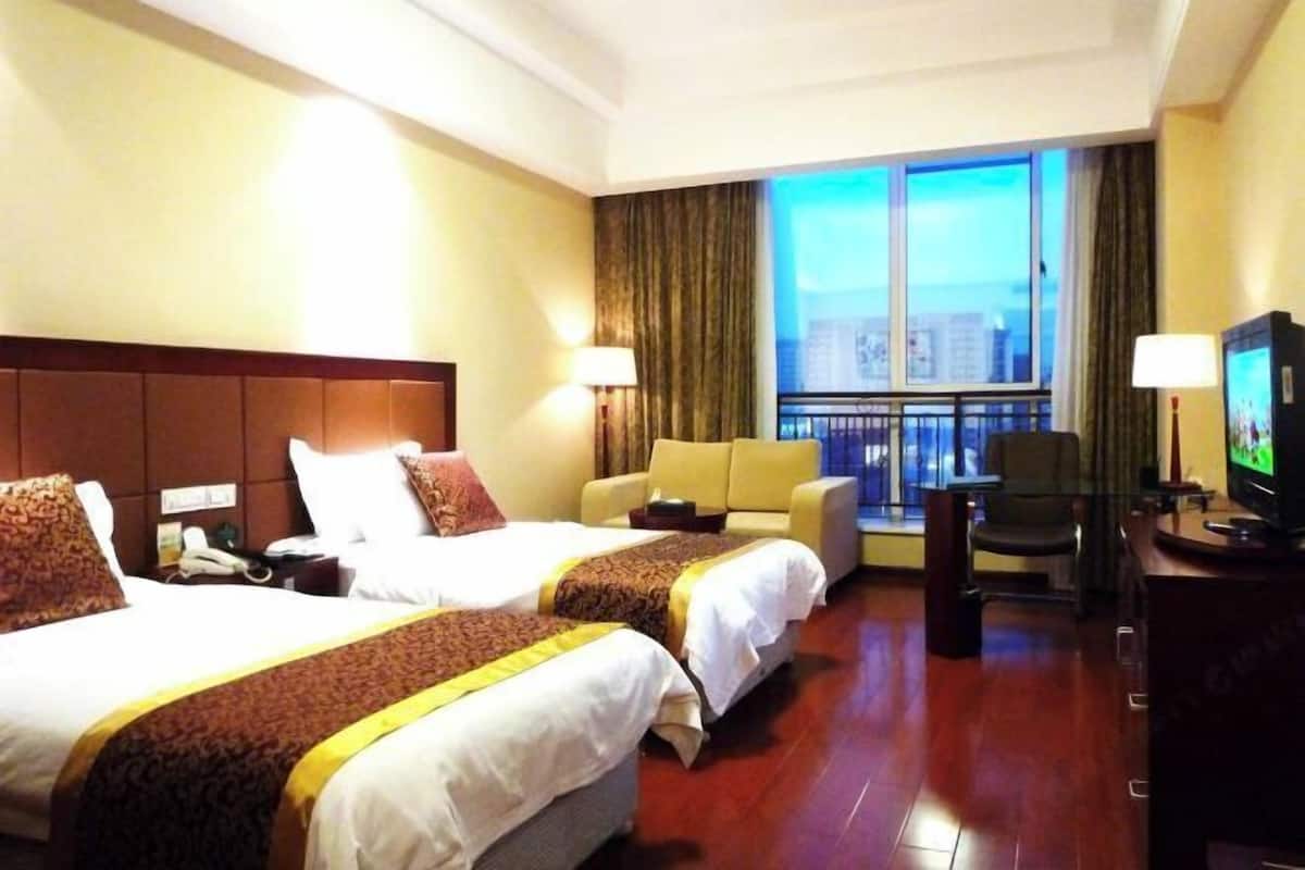 A hotel room with two beds, a sofa, a TV, and a balcony with a city view.