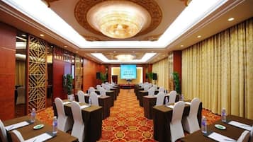 A conference room with rows of tables and chairs, a large screen at the front, and a patterned carpet.