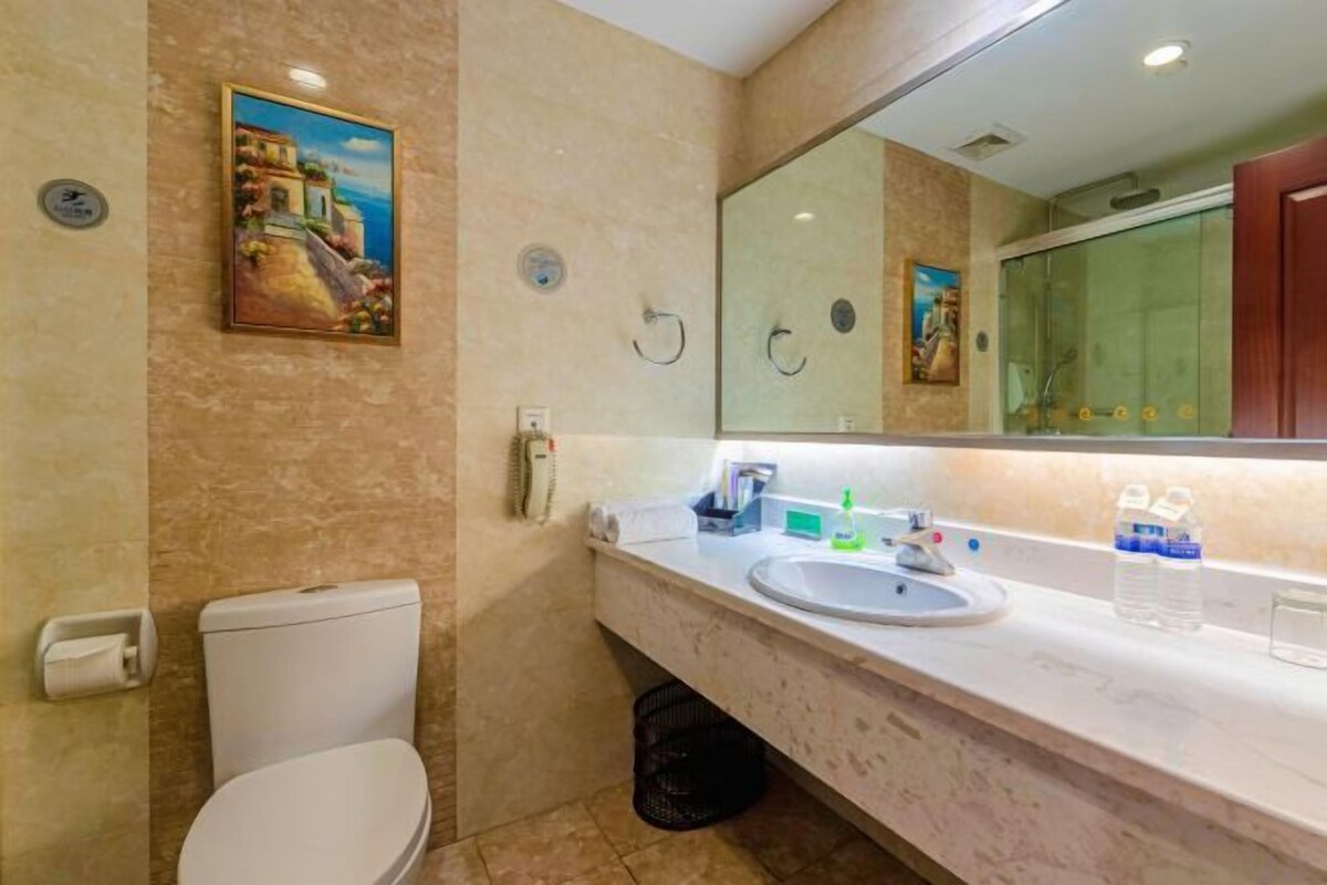 A bathroom with a toilet, sink, mirror, and a painting on the wall.
