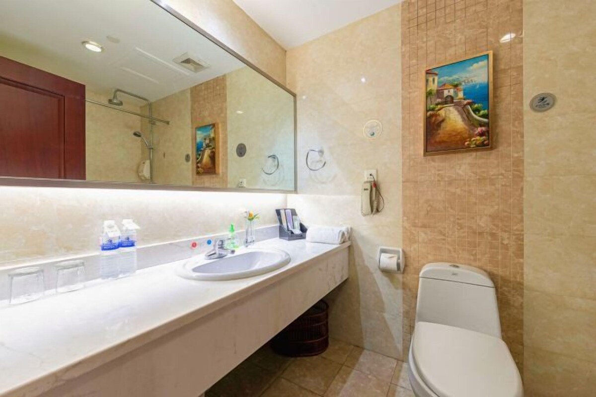 A bathroom with a large mirror, a sink, a toilet, and a painting on the wall.