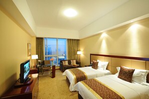 A hotel room with two beds, a desk, a television, and a view of the city through large windows. - Chengyang Detai Hotel (Qingdao)
