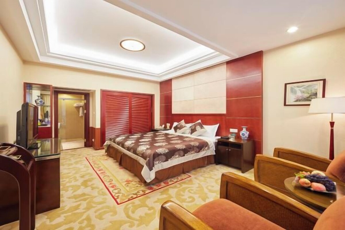 Une chambre d’hôtel avec un lit, une table de chevet, une lampe et une petite table sur laquelle sont disposés des fruits.