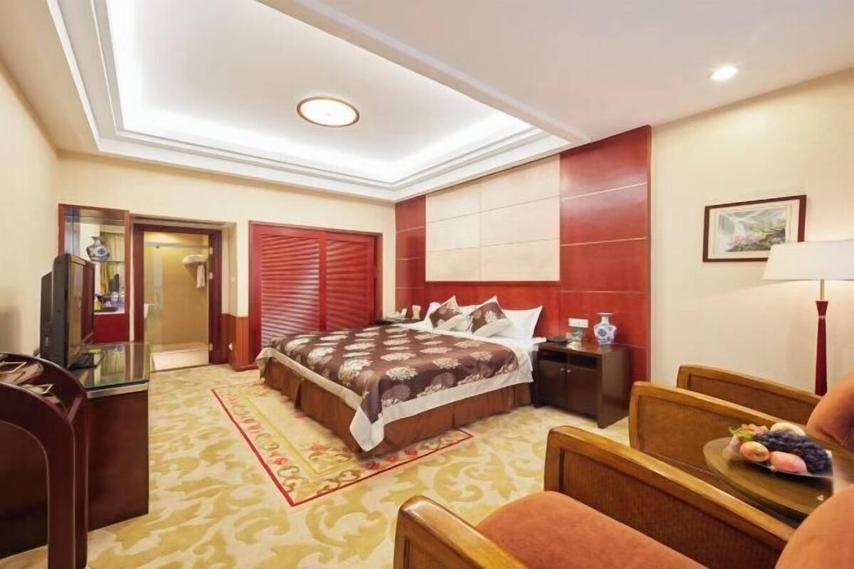 A hotel room with a bed, bedside table, lamp, and a small table with fruits.