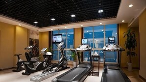 A gym with treadmills, elliptical machines, and exercise bikes, large windows, and a ceiling with a grid pattern. - Chengyang Detai Hotel (Qingdao)