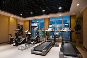 Une salle de sport Ă©quipĂ©e de tapis de course, de vĂ©los elliptiques et de vĂ©los dâexercice, dotĂ©e de grandes fenĂȘtres et dâun plafond ornĂ© dâun motif en rĂ©seau.