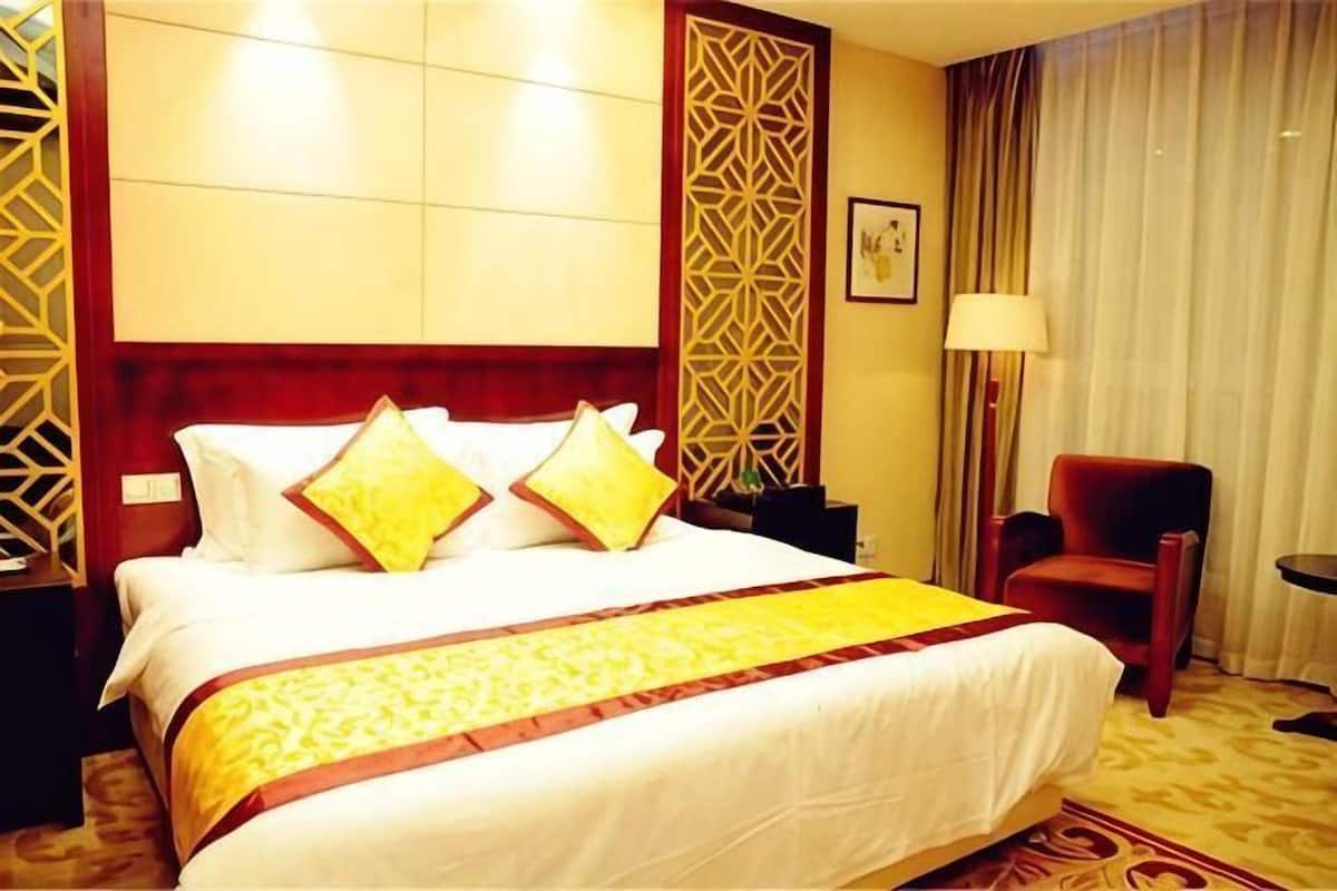 A hotel room with a large bed, a red armchair, a nightstand, and a lamp.