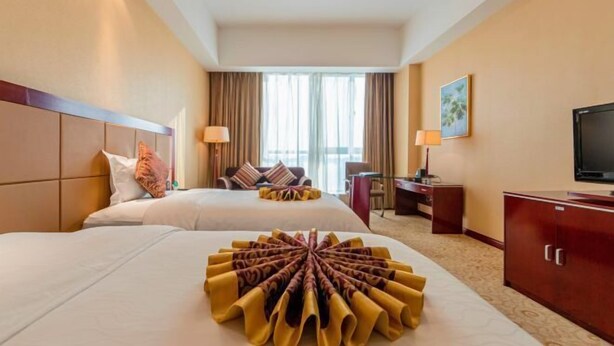 A hotel room with two beds, a desk, a television, and a large window with curtains. - Chengyang Detai Hotel (Qingdao)