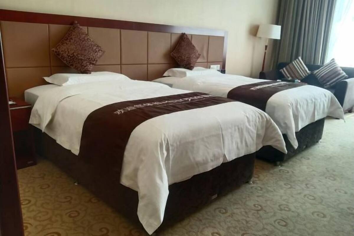 A hotel room with two beds, a headboard, a nightstand, a lamp, and a patterned carpet.