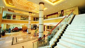 A multi-level hotel lobby with a central staircase, glass railings, and a patterned floor. - Chengyang Detai Hotel (Qingdao)