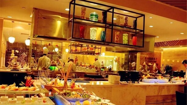 A buffet with various food items, a kitchen area with chefs, and a dining area with tables and chairs. - Chengyang Detai Hotel (Qingdao)
