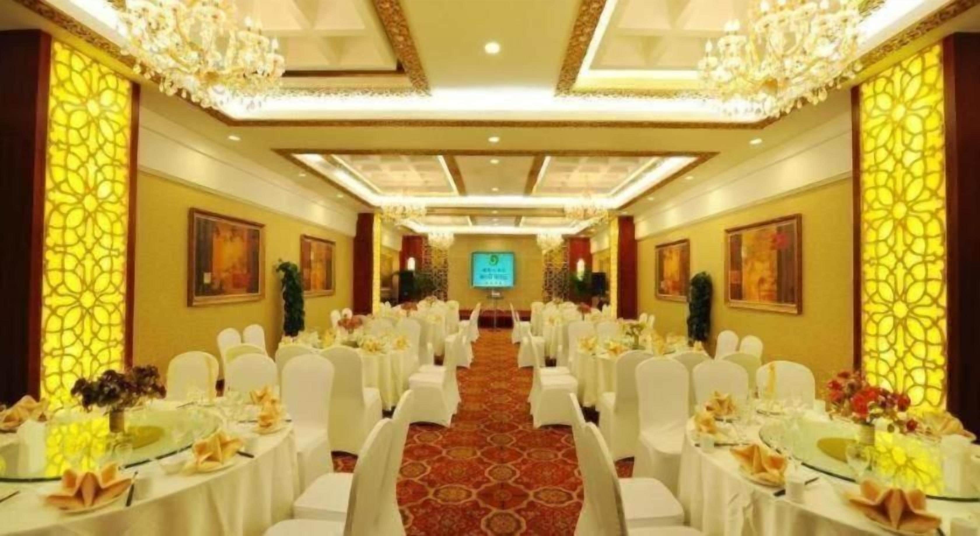 Un salón de banquetes con filas de mesas, sillas blancas y candelabros.