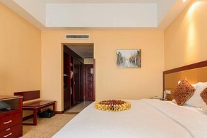 A hotel room with a bed, a desk, a chair, a painting, and a door leading to another room. - Chengyang Detai Hotel (Qingdao)