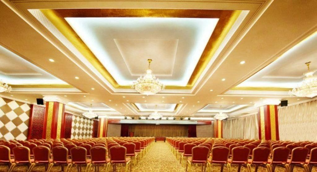 Un salón de conferencias con filas de sillas, un escenario y una lámpara de araña.