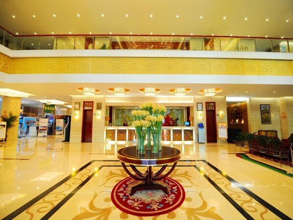 A hotel lobby with a reception desk, a round table with vases, and a high ceiling with a balcony. - Chengyang Detai Hotel (Qingdao)