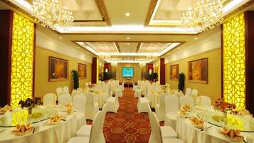 Un salón de banquetes con mesas redondas, sillas blancas, candelabros y suelo alfombrado.