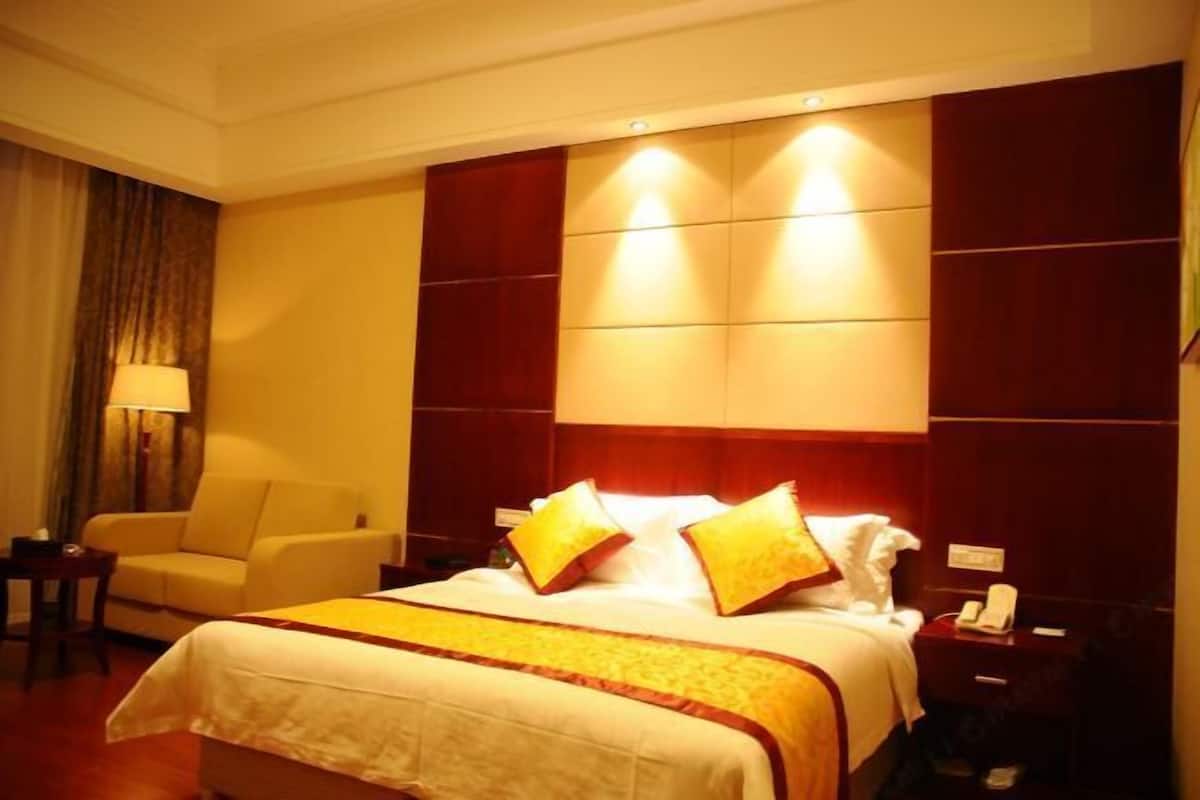 A hotel room with a large bed, a bedside table, a lamp, a chair, and a wardrobe.