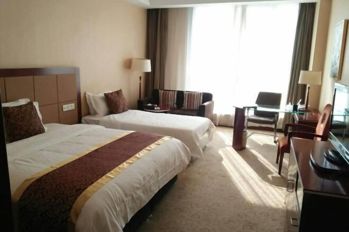 A hotel room with two beds, a desk, a chair, and a TV.