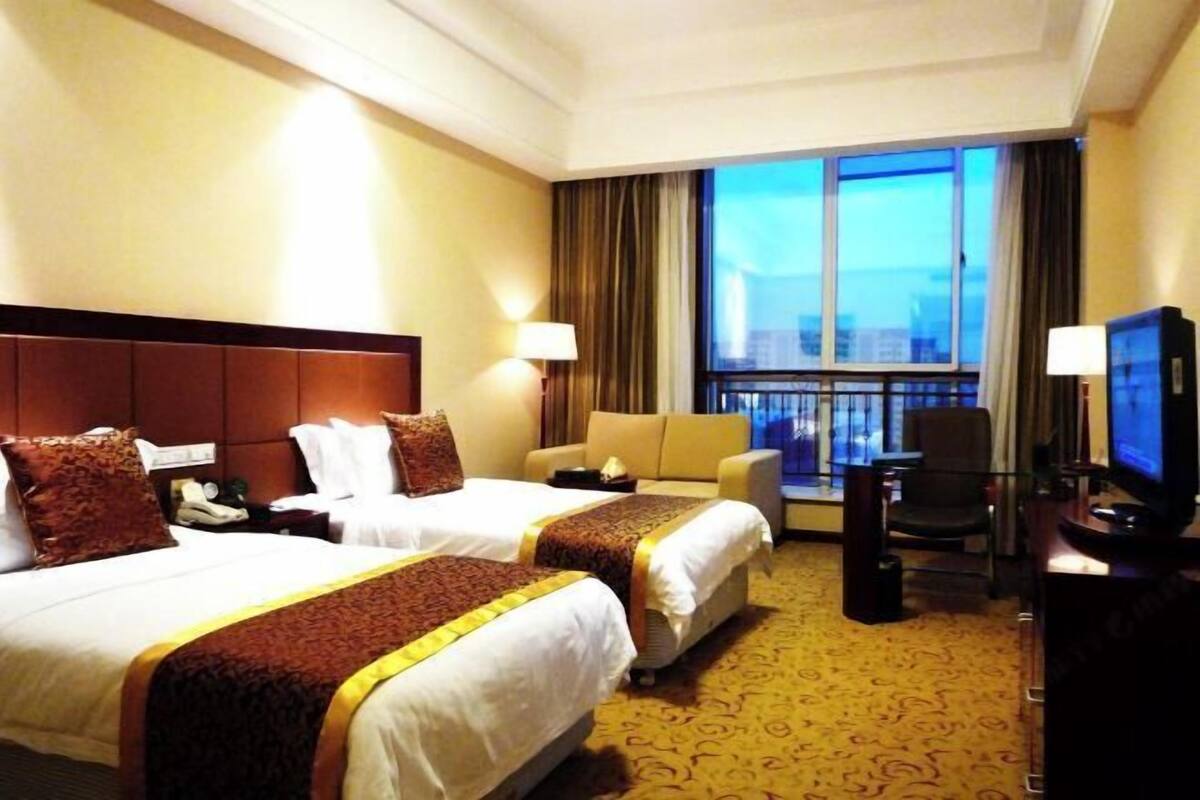 A hotel room with two beds, a sofa, a TV, and a large window with a city view.