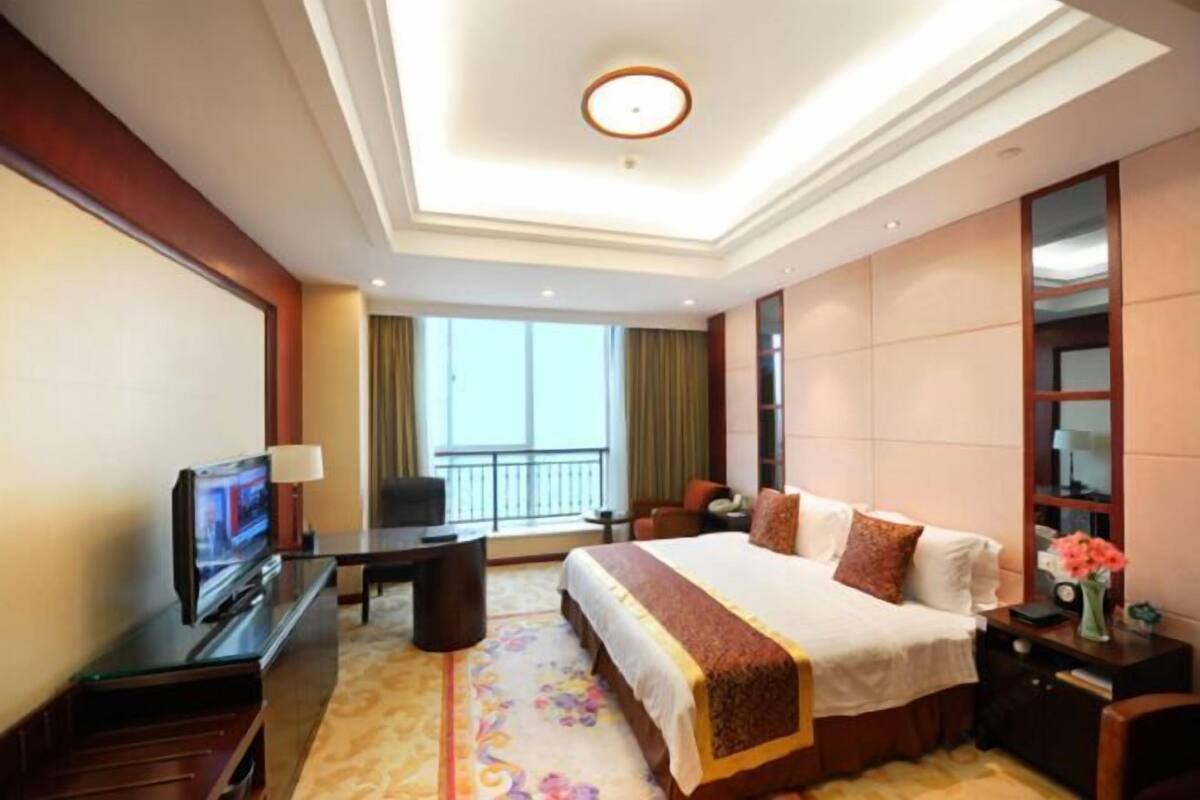 A hotel room with a bed, a desk, a television, a chair, a balcony view, and a large mirror.
