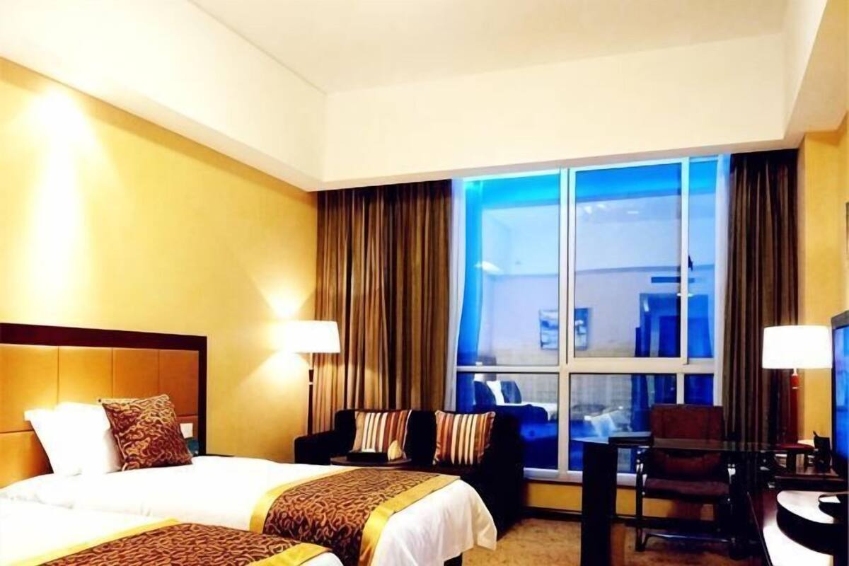 A hotel room with a large bed, a desk, a chair, and a window with curtains.
