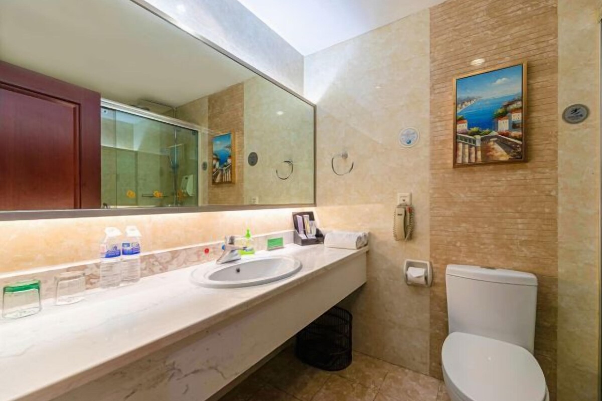 A bathroom with a marble sink, a toilet, a large mirror, and a painting on the wall.