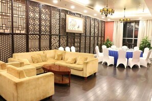 A room with a sectional sofa, a round coffee table, and a dining area with a blue tablecloth and white chairs. - Excemon Beijing Hongxiang Hotel (Beijing)