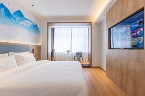Une chambre d’hôtel avec un grand lit, un téléviseur fixé au mur et une vue sur l’extérieur par une fenêtre.