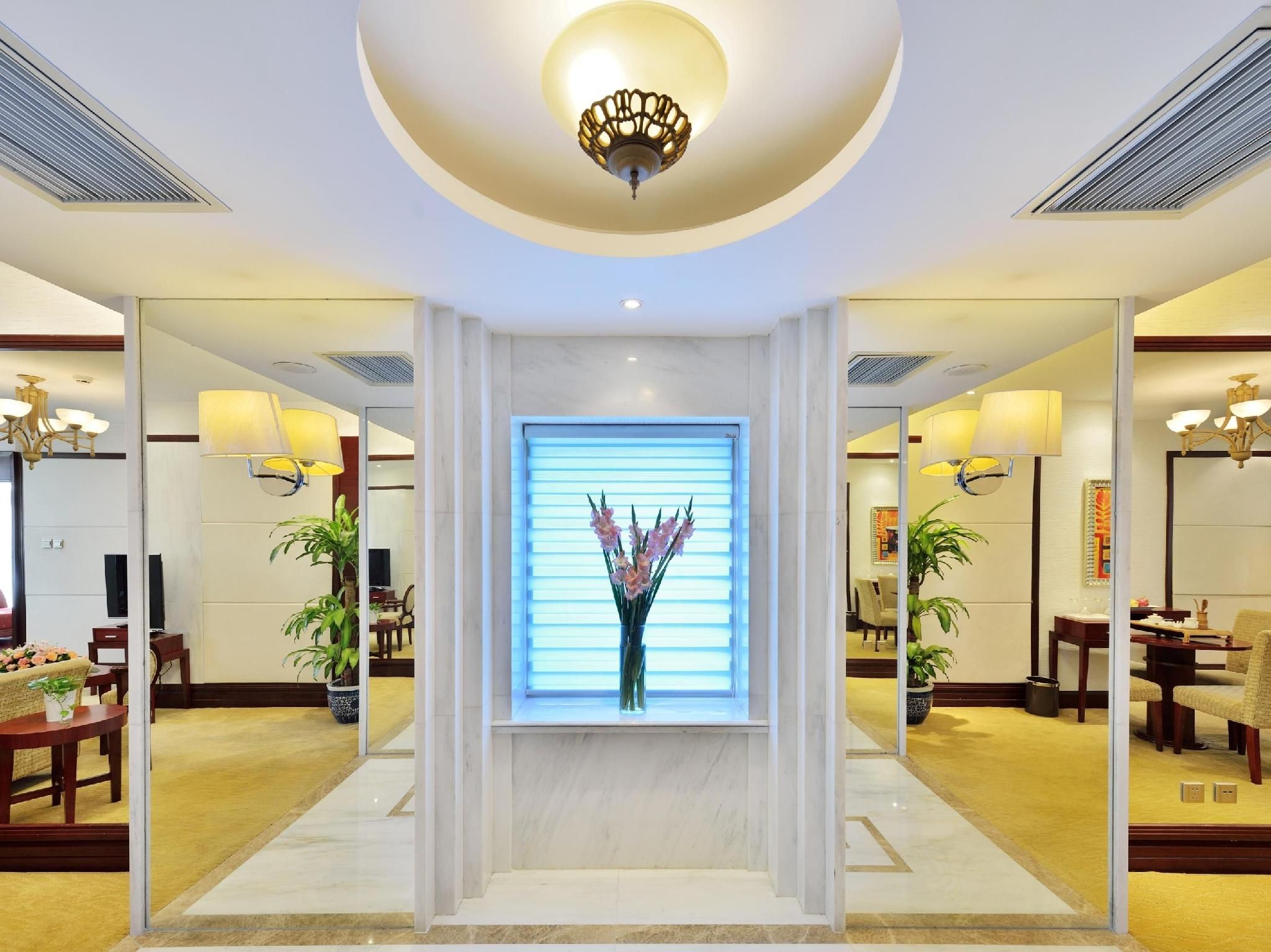 A hotel lobby with a central reception desk, a large window with blinds, and multiple seating areas.