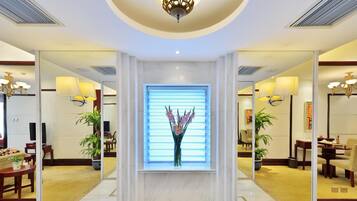 A hotel lobby with a central reception desk, a large window with blinds, and multiple seating areas.