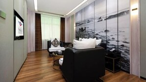 Une chambre d’hôtel moderne avec un canapé noir, une petite table ronde et une grande fresque murale représentant un paysage rocheux.