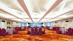 Une salle de conférence dotée d’une grande table ovale, entourée de chaises violettes, d’un tapis à motifs et d’un plafond agrémenté d’un éclairage géométrique.