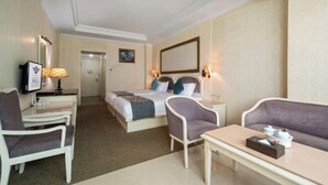 Une chambre d’hôtel comprenant un lit, deux tables de chevet, une chaise, un canapé et une petite table avec un plateau.