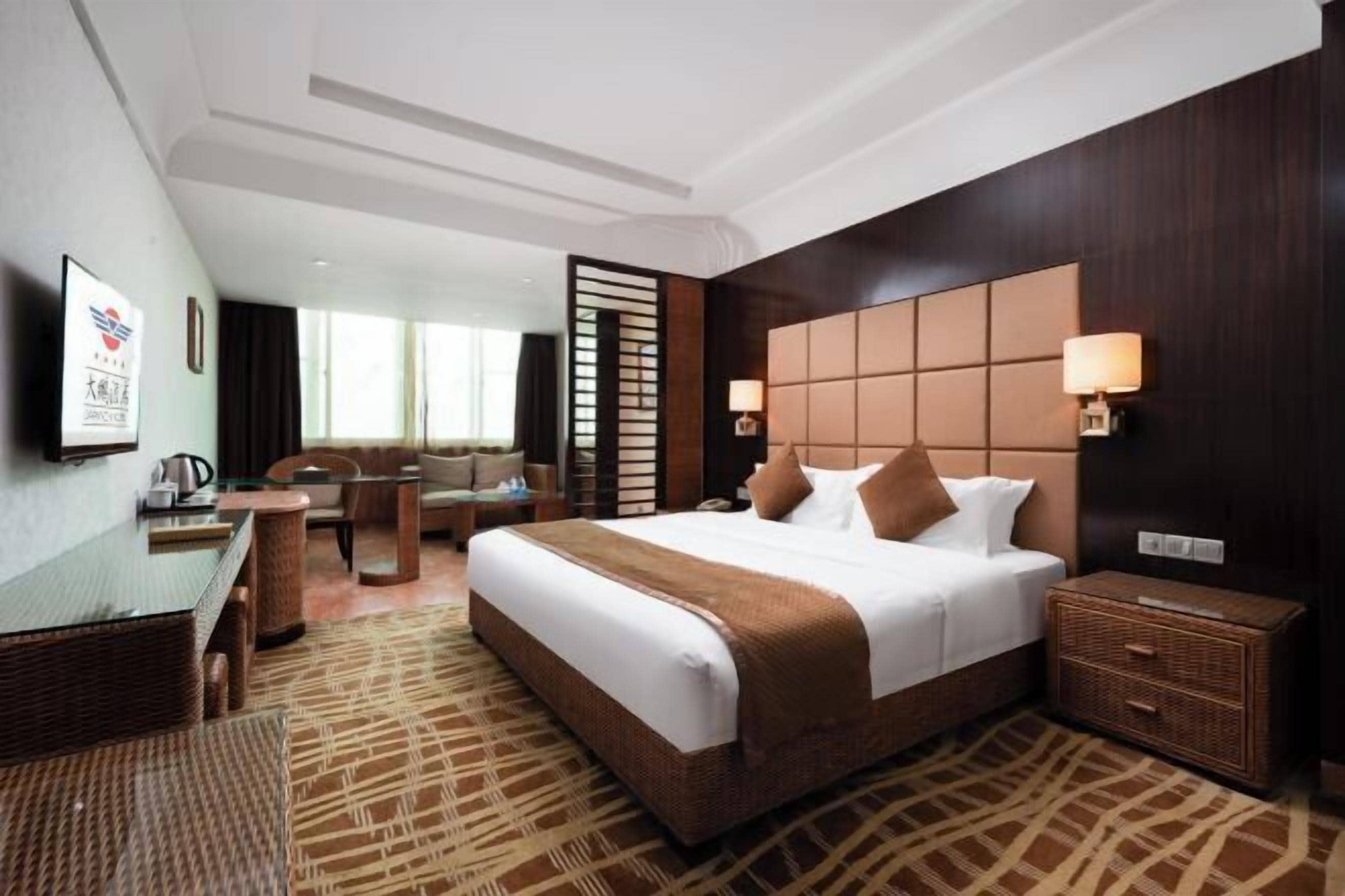 A hotel room with a large bed, a desk, a chair, a sofa, a TV, and a window.