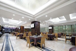 A spacious restaurant with multiple tables and chairs, a high ceiling with skylights, and a modern design.