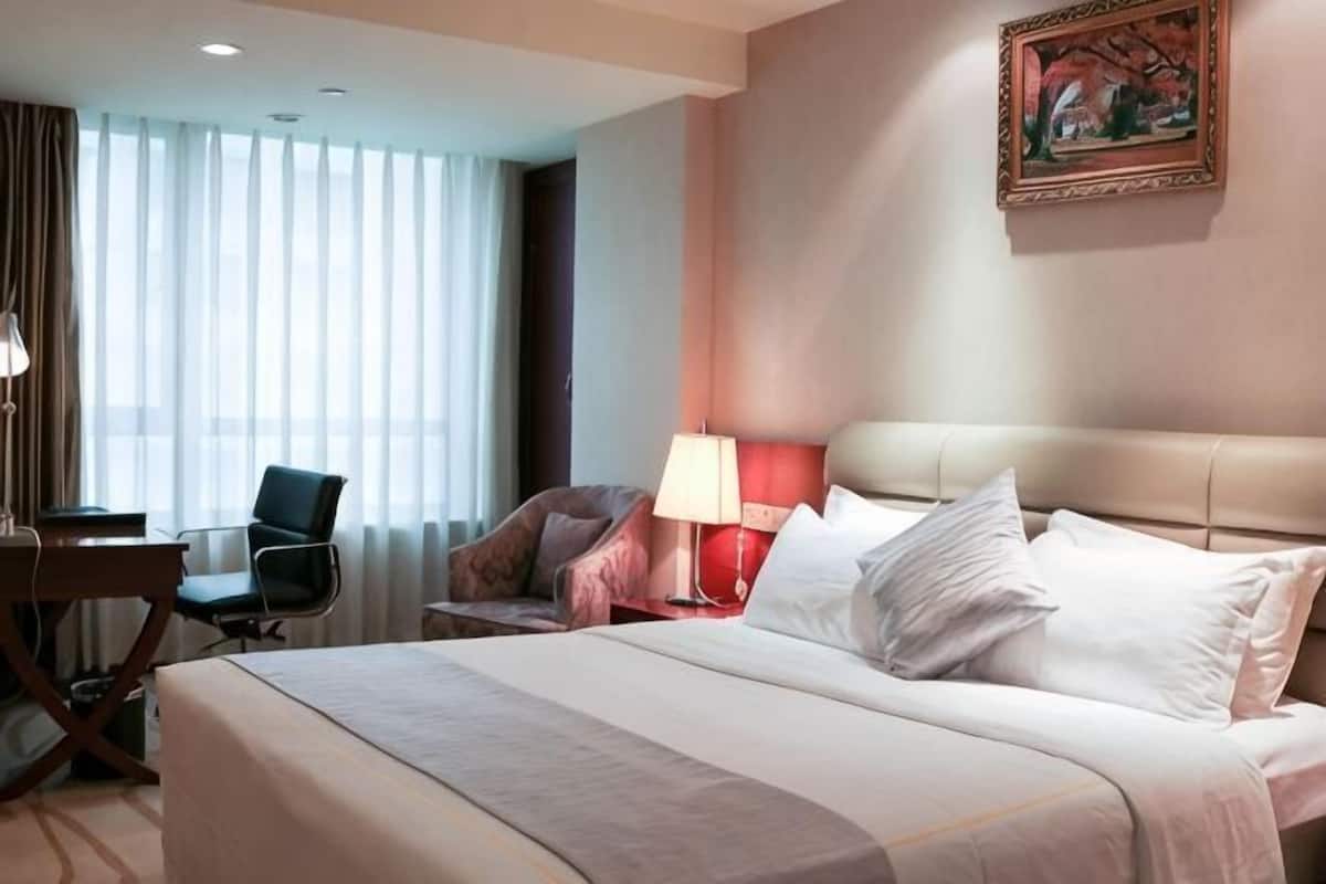 Et hotelværelse med en seng, to stole, et skrivebord, en lampe og et billede på væggen.