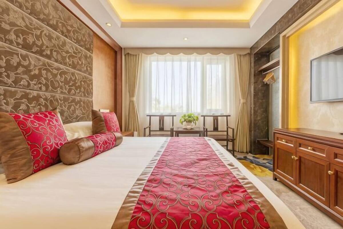 A hotel room with a large bed, a TV, a dining table, and a sofa.