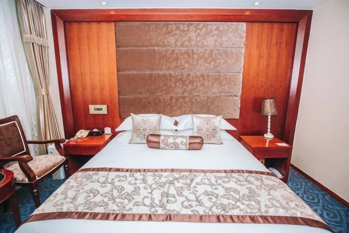 A hotel room with a large bed, wooden headboard, a desk with a telephone, a chair, and a lamp.