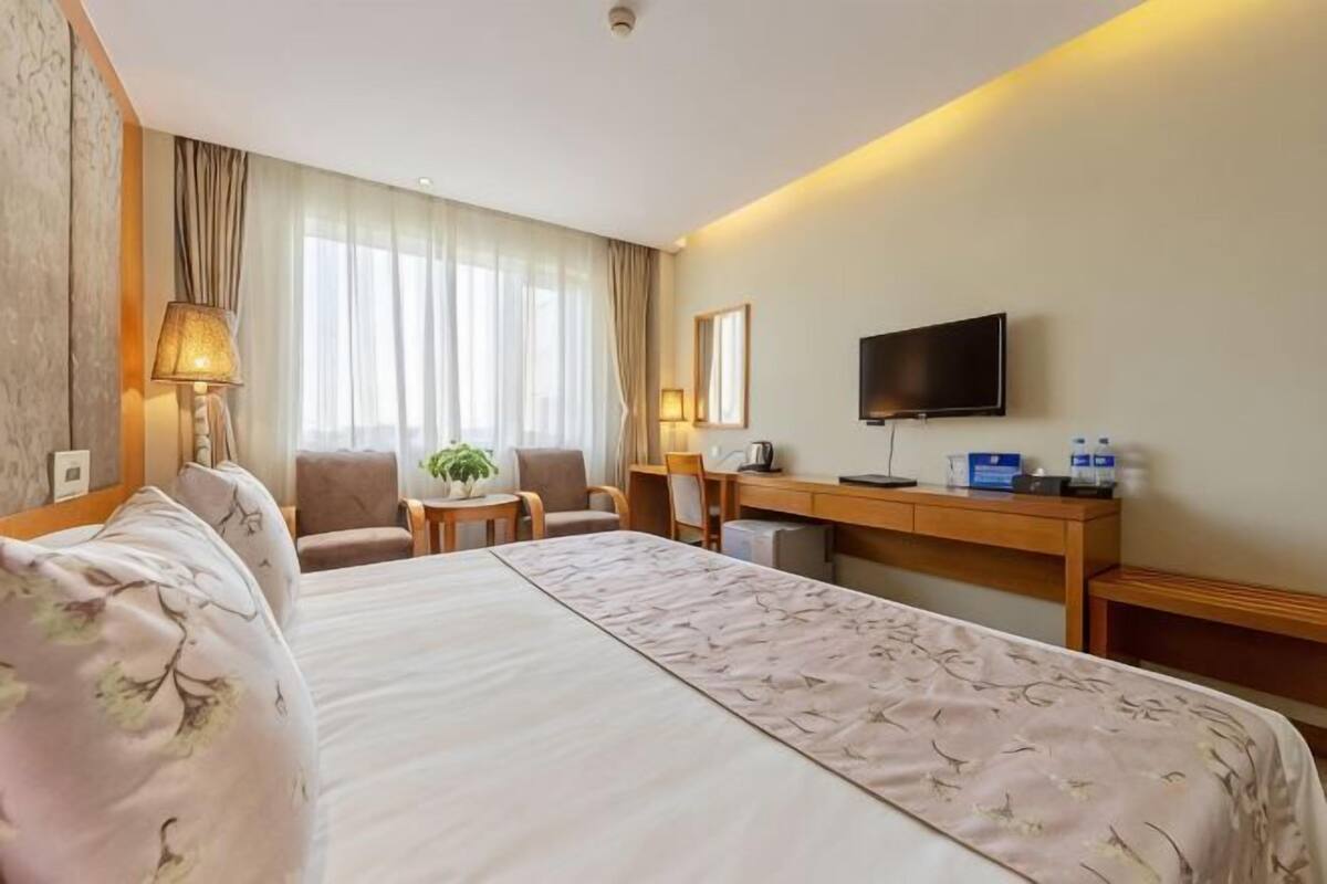 A hotel room with a bed, a desk, a chair, a TV, and a window with curtains.