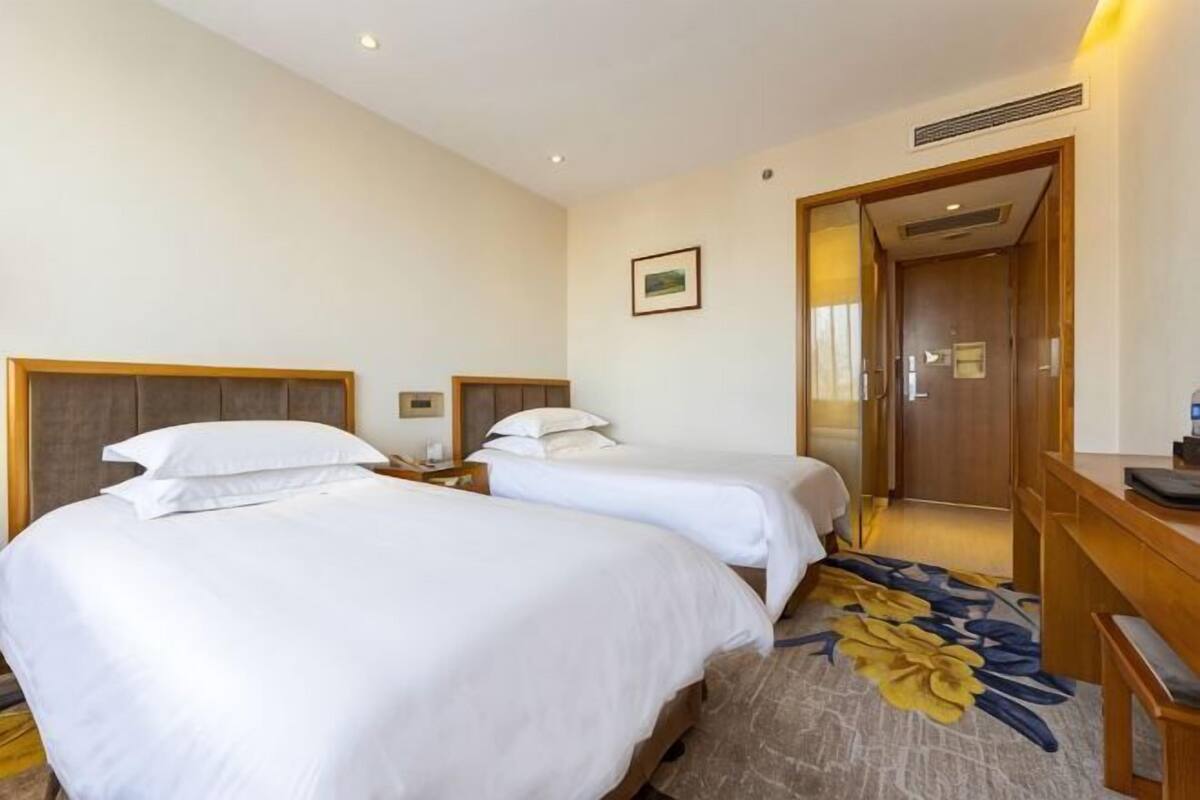 A hotel room with two beds, a wooden desk, a nightstand, and a door leading to another room.